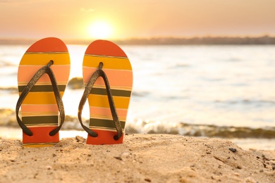 Photo of Stylish flip flops on sand near sea, space for text. Beach accessories