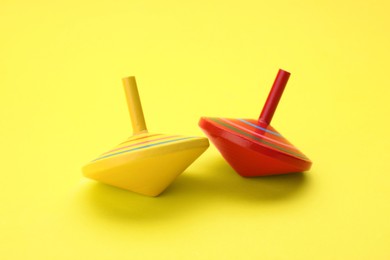 Photo of Two bright spinning tops on yellow background. Toy whirligig