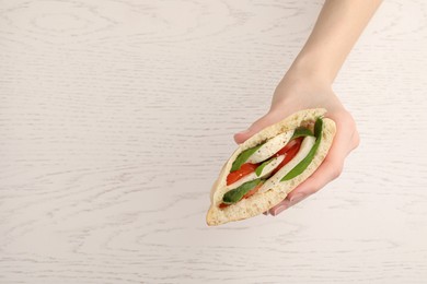 Photo of Woman holding delicious pita sandwich with mozzarella, tomatoes and basil at white wooden table, closeup. Space for text