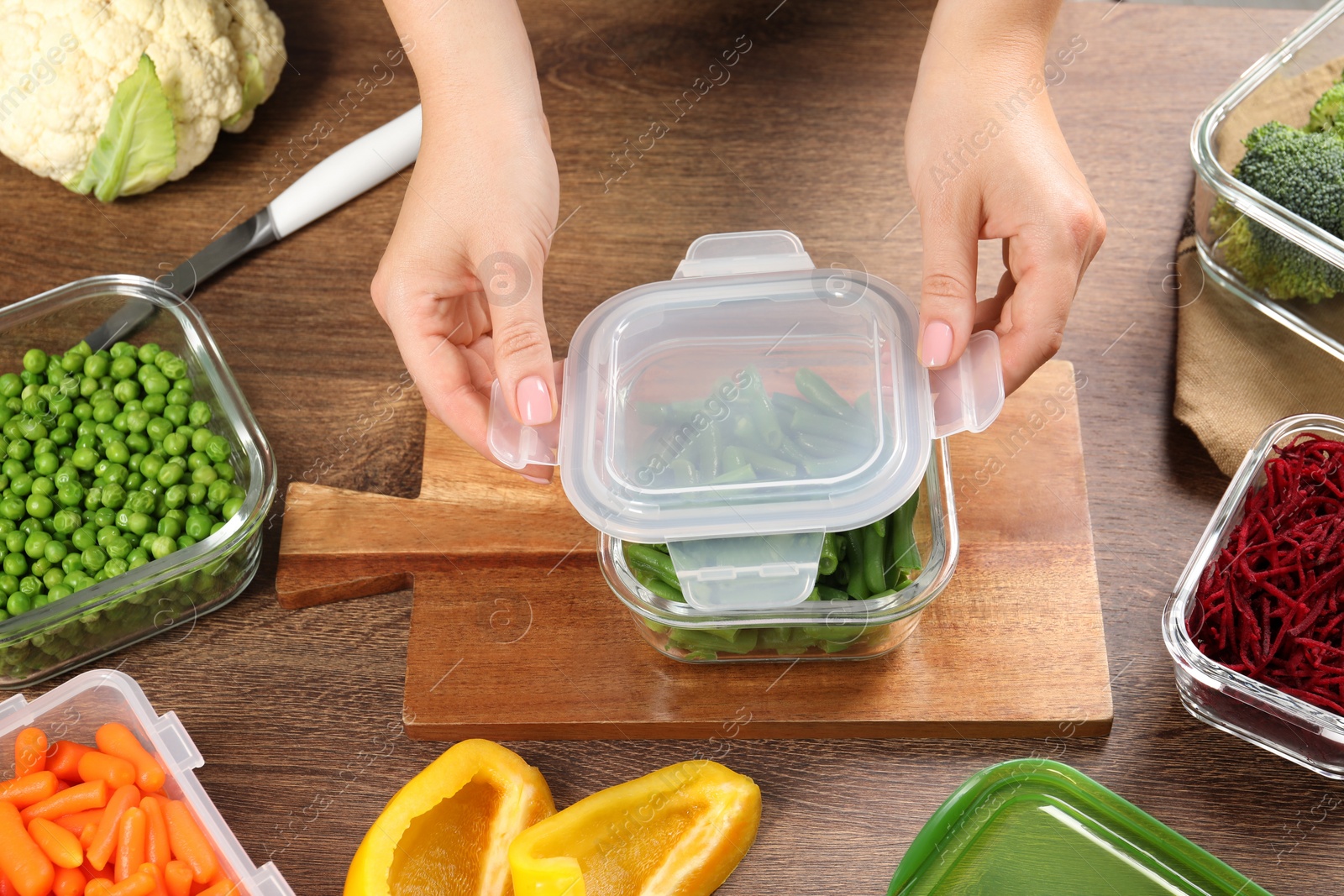 Photo of Woman closing container with lid at wooden table, above view. Food storage