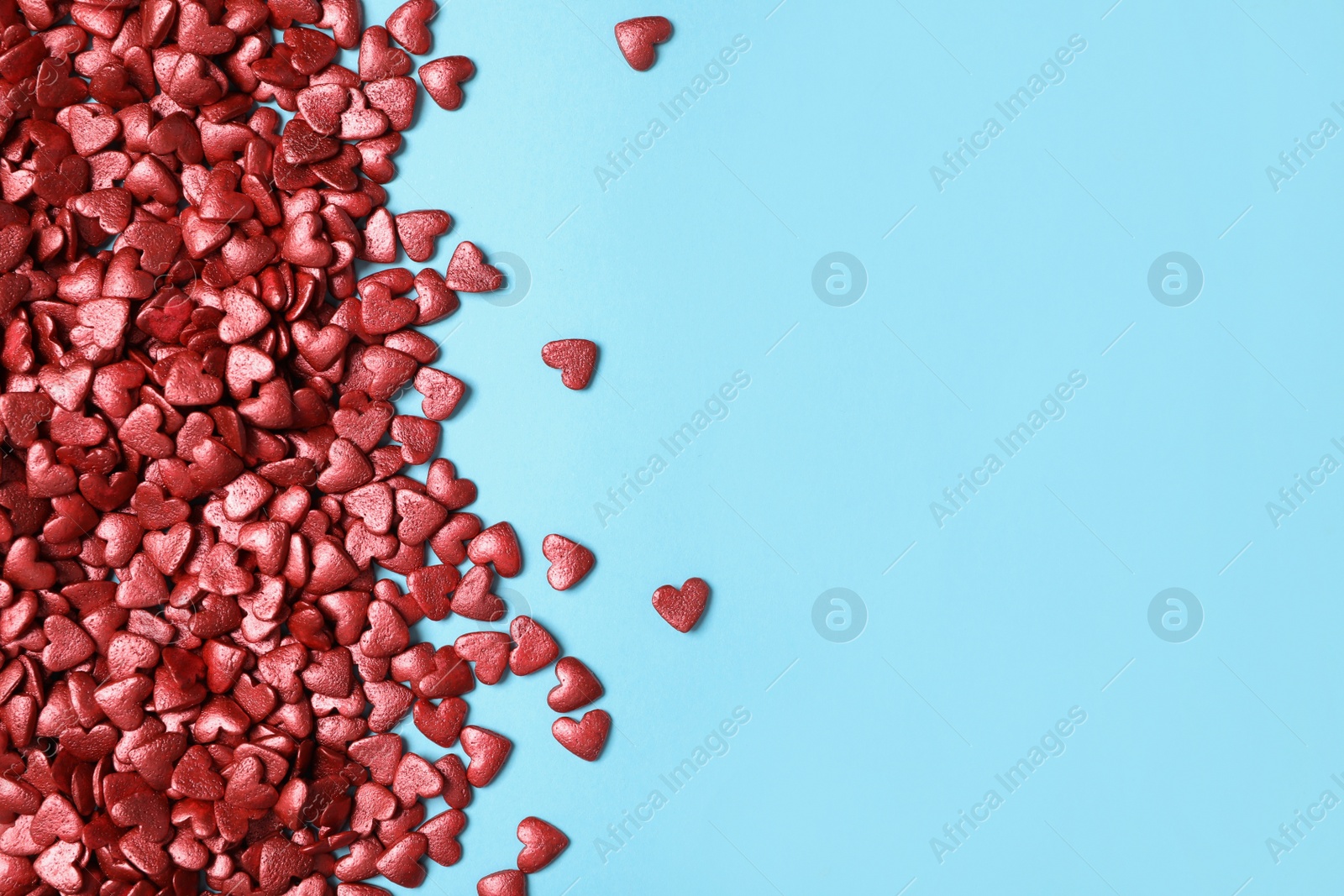 Photo of Bright heart shaped sprinkles on light blue background, flat lay. Space for text