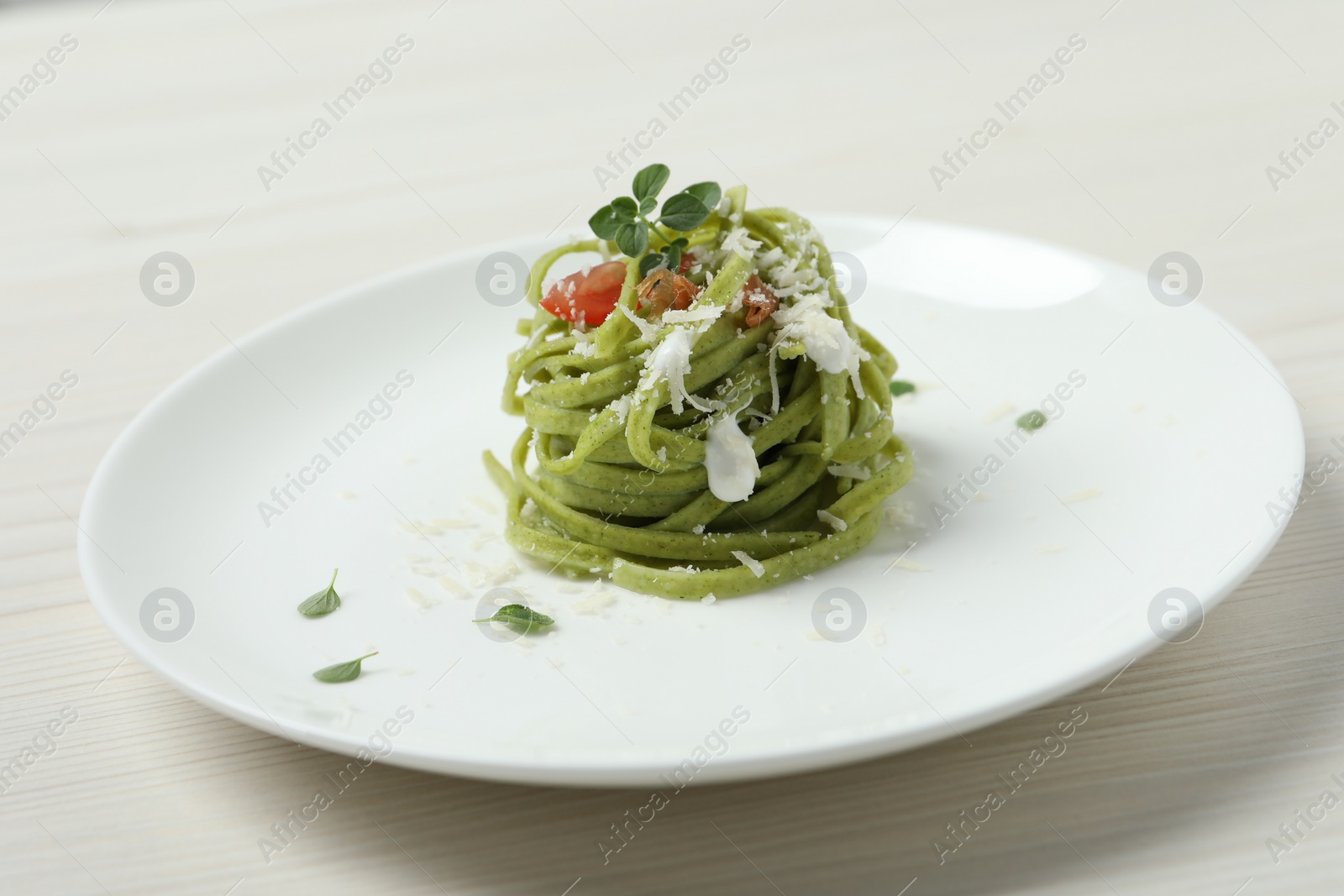 Photo of Tasty tagliatelle with spinach and cheese served on white wooden table, closeup. Exquisite presentation of pasta dish