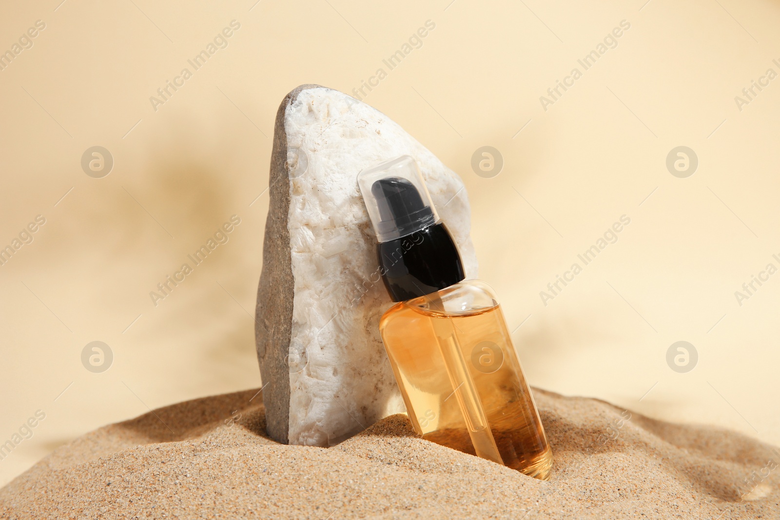 Photo of Bottle of serum and stone on sand against beige background