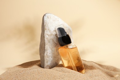 Photo of Bottle of serum and stone on sand against beige background