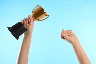 Photo of Woman holding gold trophy cup on light blue background, closeup