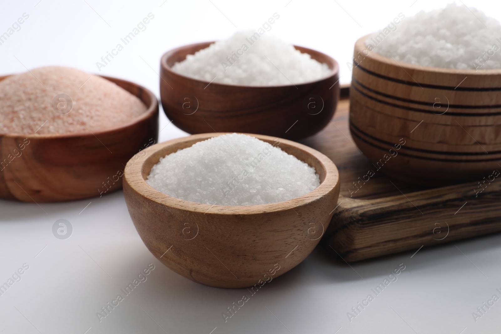 Photo of Different types of natural salt in wooden bowls on white background