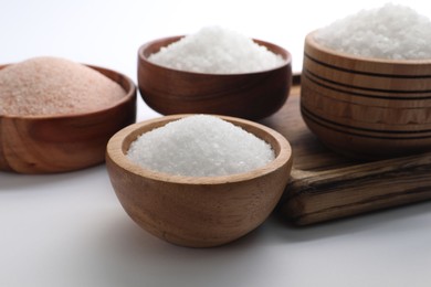 Photo of Different types of natural salt in wooden bowls on white background