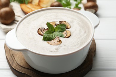 Photo of Fresh homemade mushroom soup in ceramic pot on white wooden table, closeup