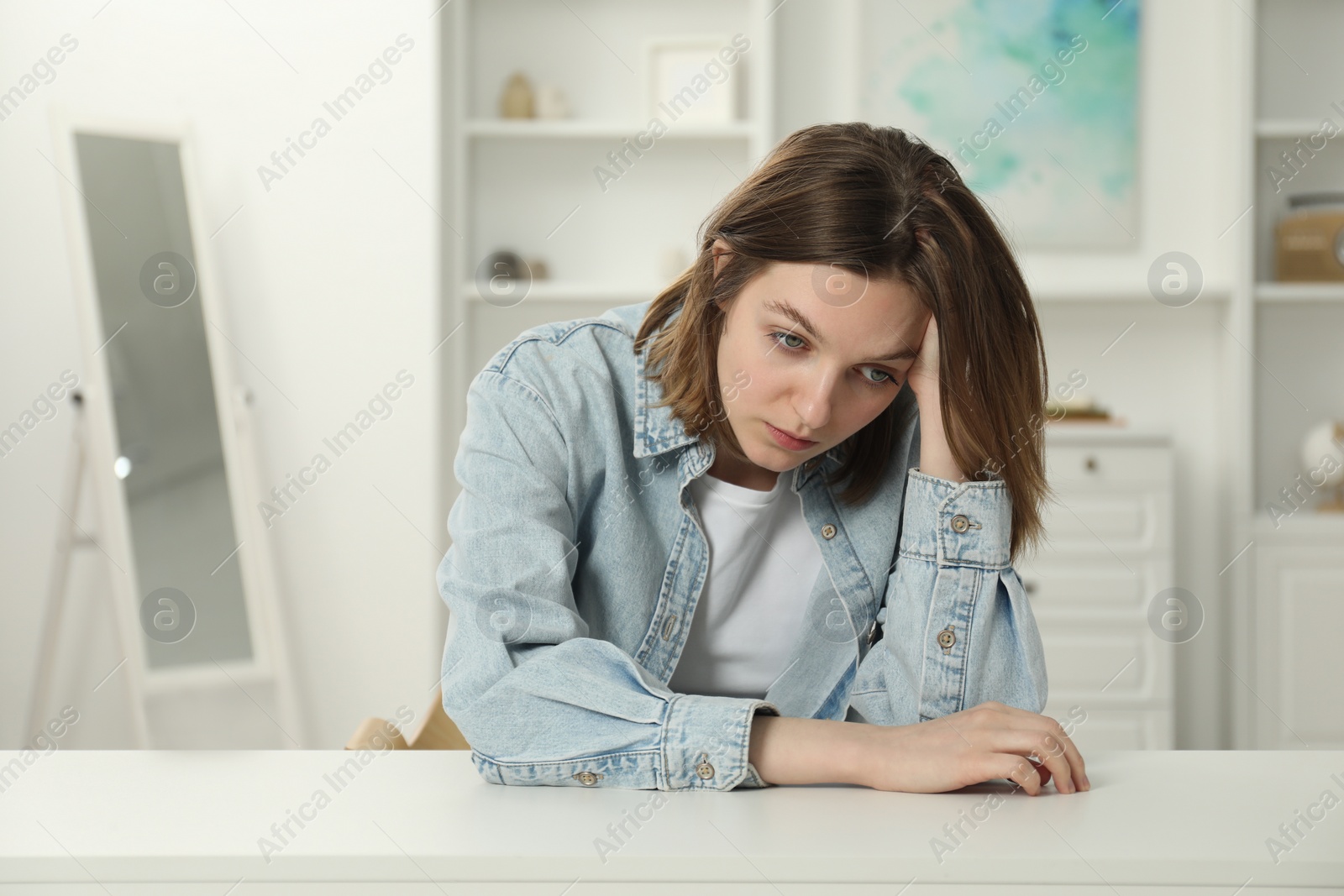 Photo of Sad young woman sitting at white table in room