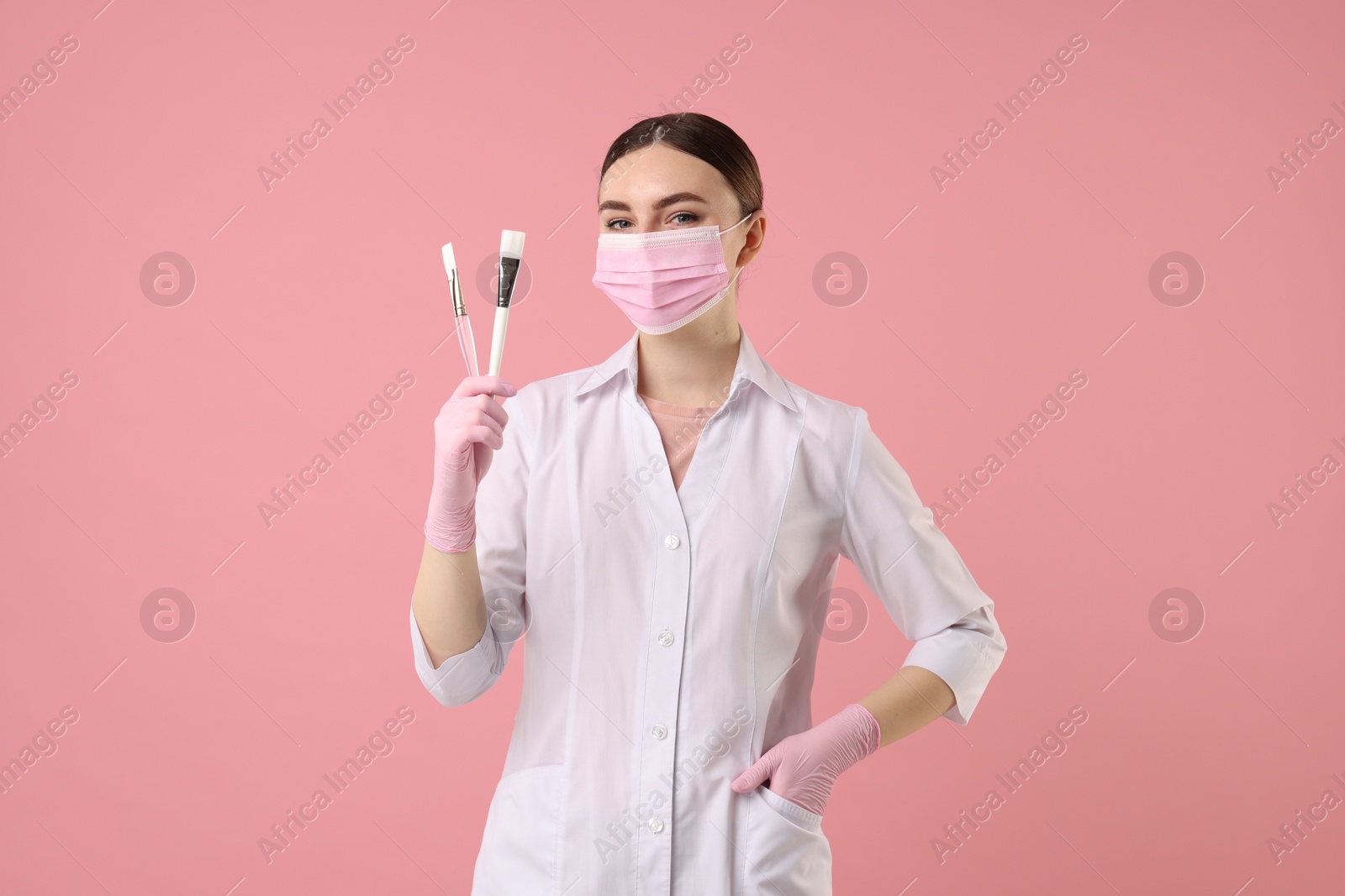 Photo of Cosmetologist with cosmetic brushes on pink background