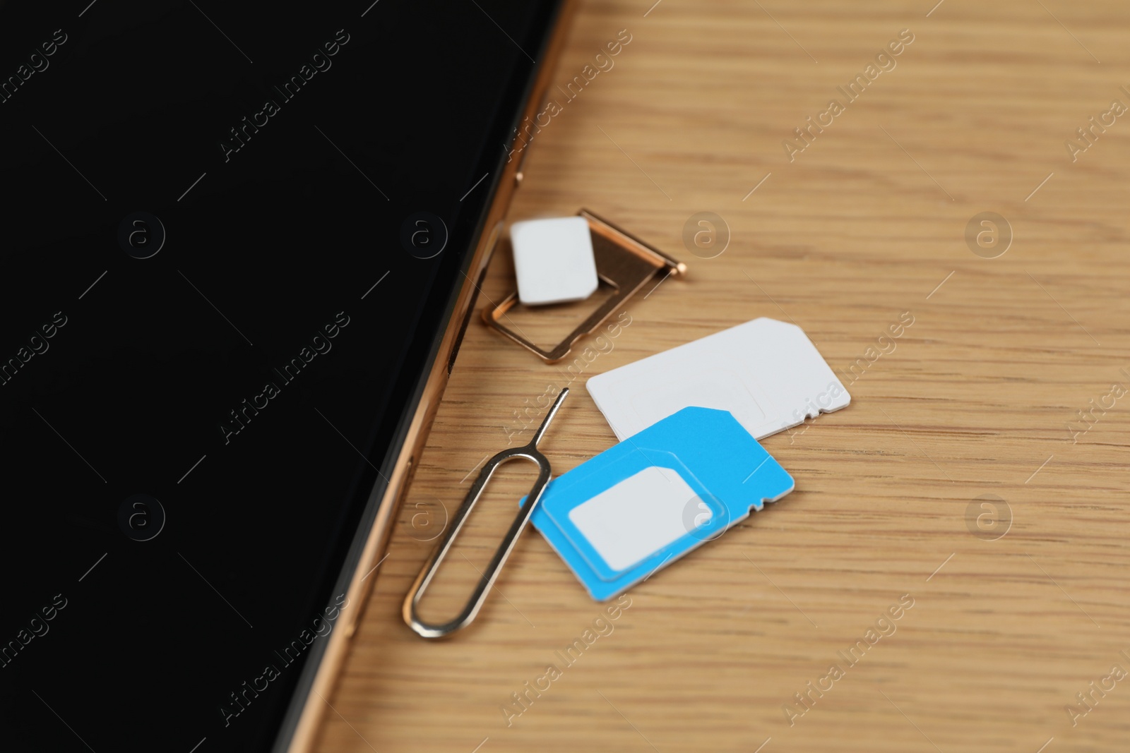 Photo of SIM cards, mobile phone and ejector tool on wooden table, closeup