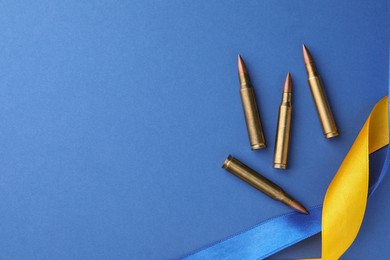 Photo of Ribbons in colors of national Ukrainian flag and bullets on blue background, flat lay. Space for text
