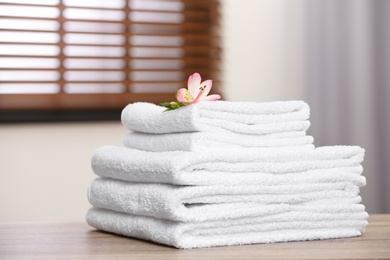 Photo of Pile of fresh towels and flower on wooden table in room