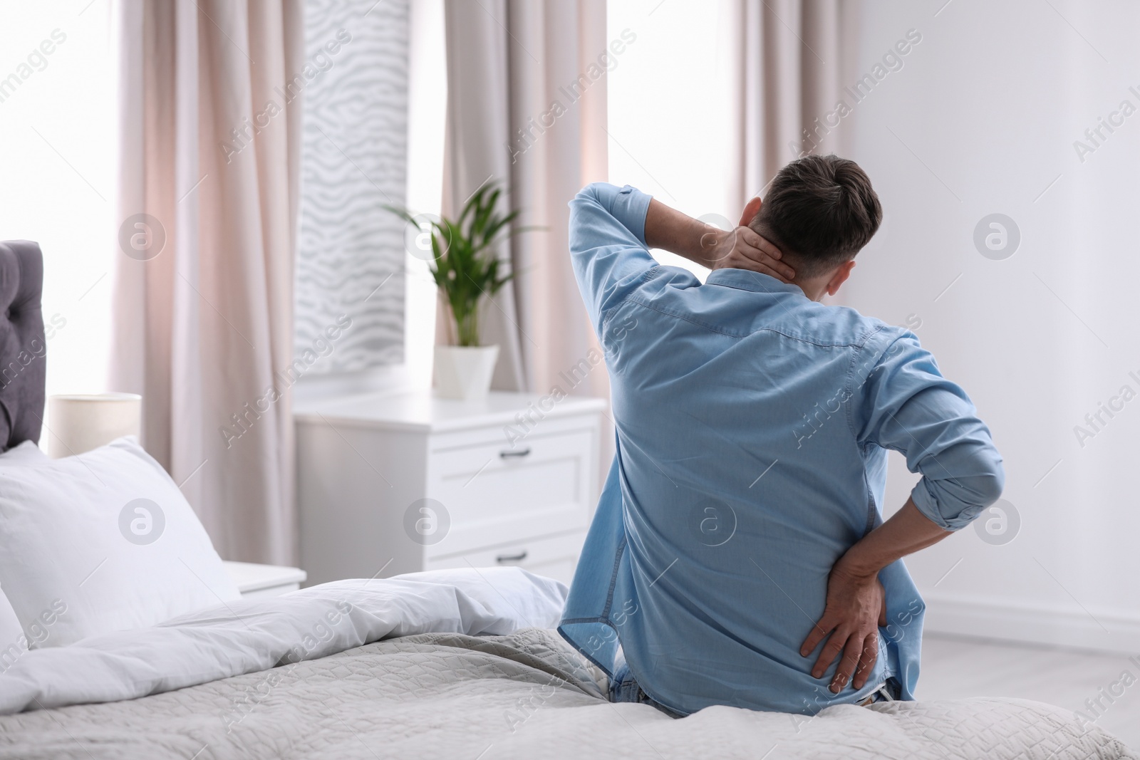 Photo of Young man suffering from back pain at home