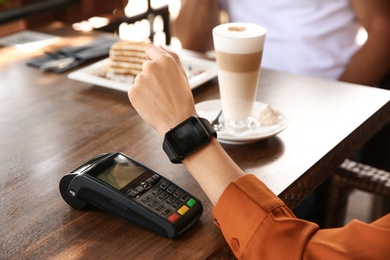 Photo of Woman making payment with smart watch in cafe, closeup