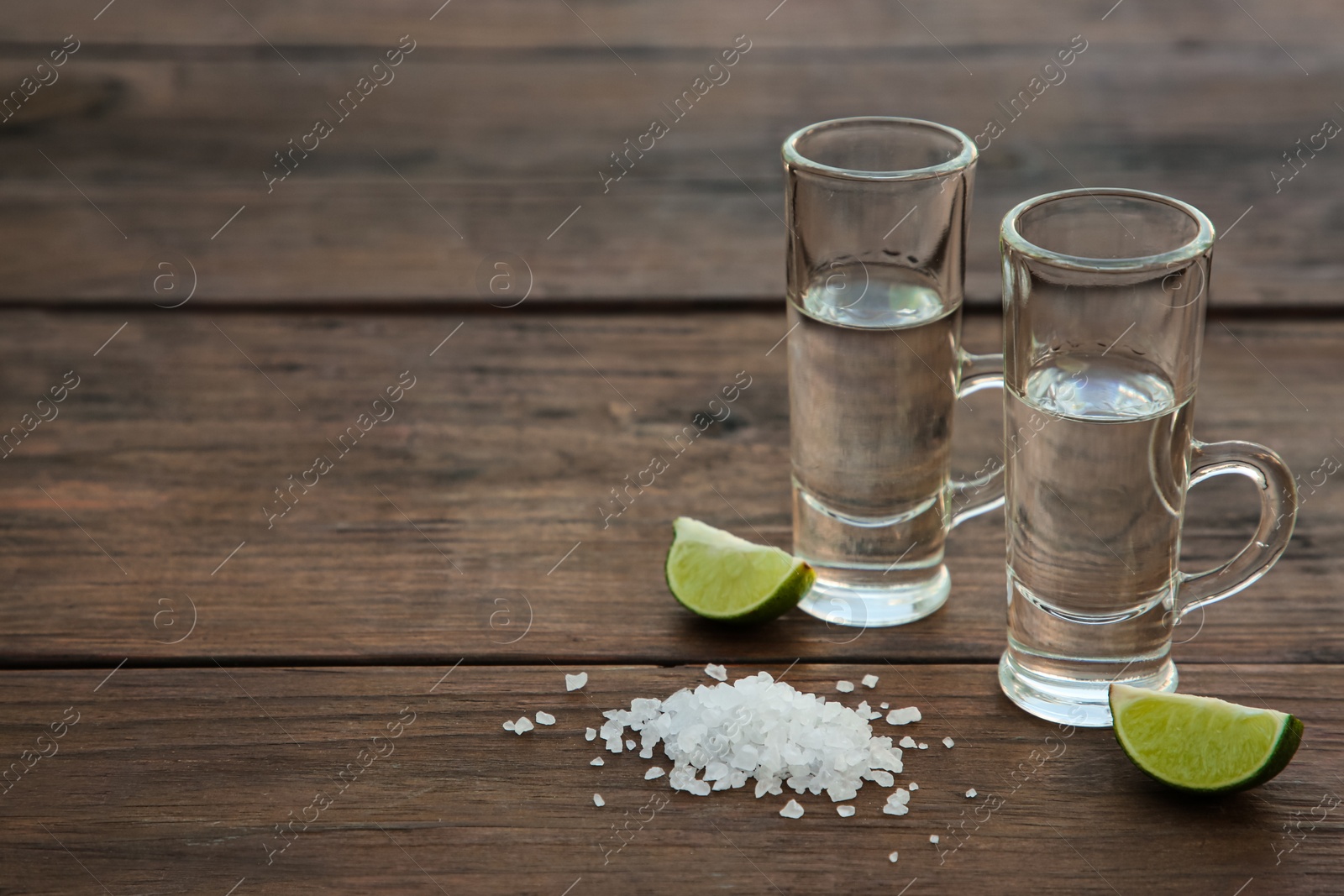 Photo of Mexican tequila shots with lime slices and salt on wooden table. Space for text