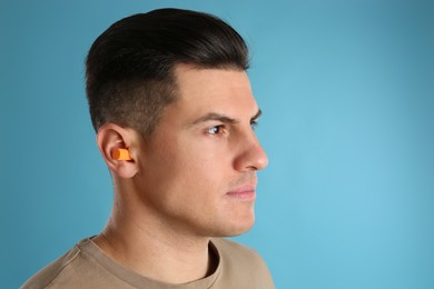 Man wearing foam ear plugs on light blue background