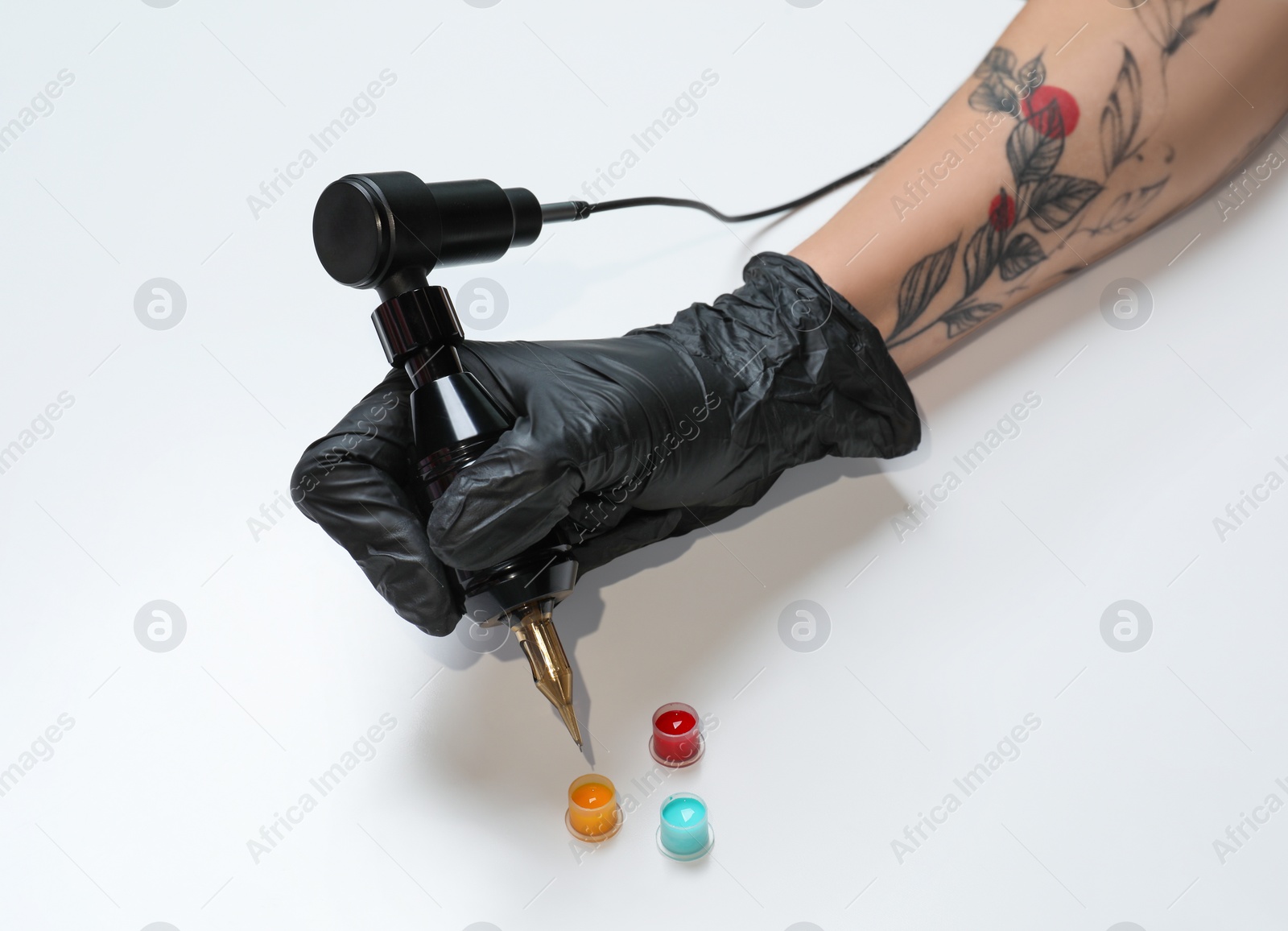 Photo of Tattoo artist with professional machine and colorful ink on white background, closeup