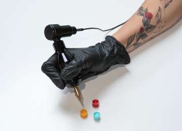 Tattoo artist with professional machine and colorful ink on white background, closeup