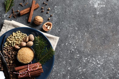 Different aromatic spices and fir branches on grey textured table, flat lay. Space for text