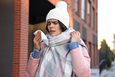 Photo of Woman with tissue blowing runny nose outdoors. Cold symptom