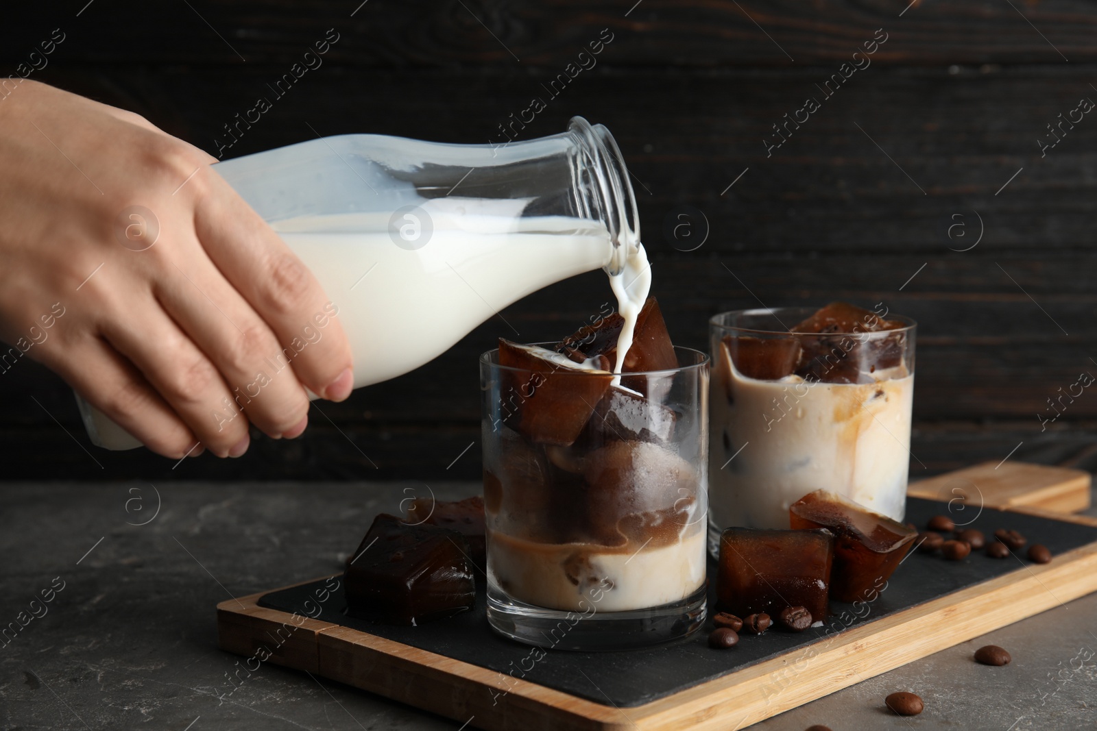 Photo of Woman pouring milk into glass with coffee ice cubes on table