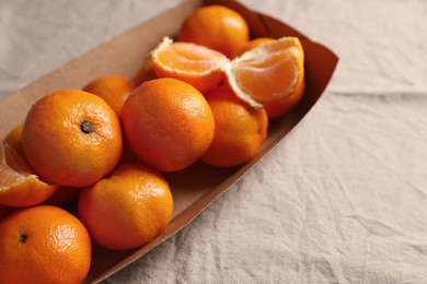 Photo of Paper box with fresh ripe tangerines on beige cloth, closeup. Space for text