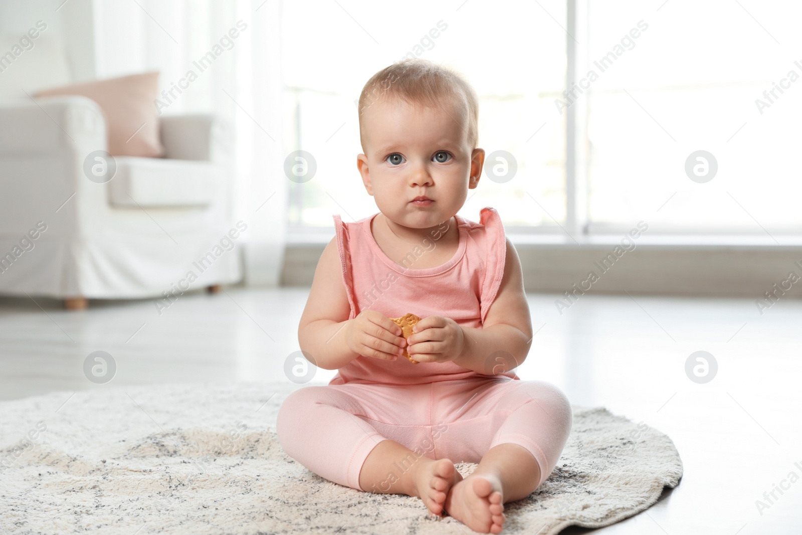 Photo of Cute baby girl with cookie on floor in room