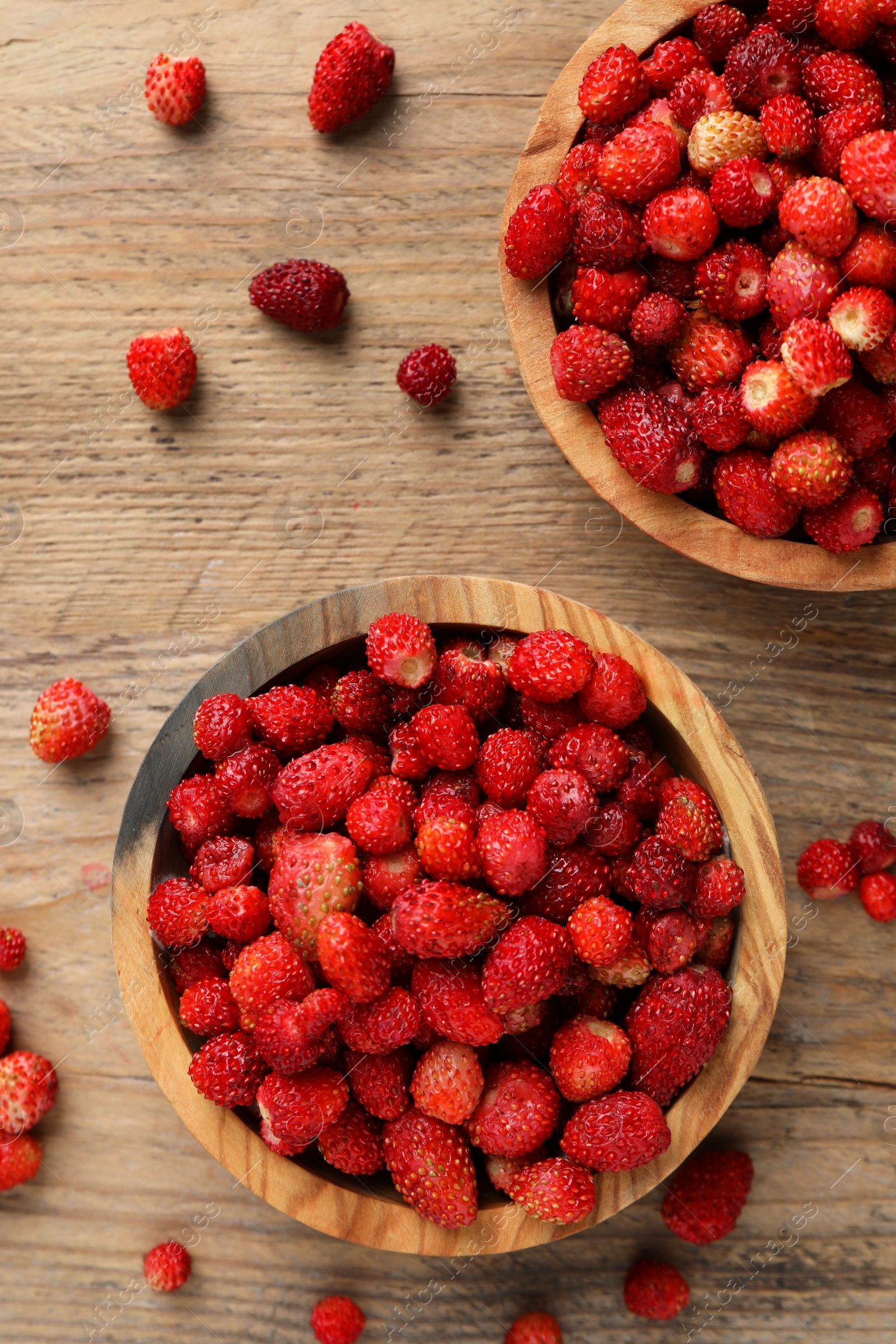 Photo of Fresh wild strawberries in bowls on wooden table, flat lay