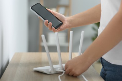 Photo of Woman with smartphone connecting cable to Wi-Fi router at table indoors, closeup