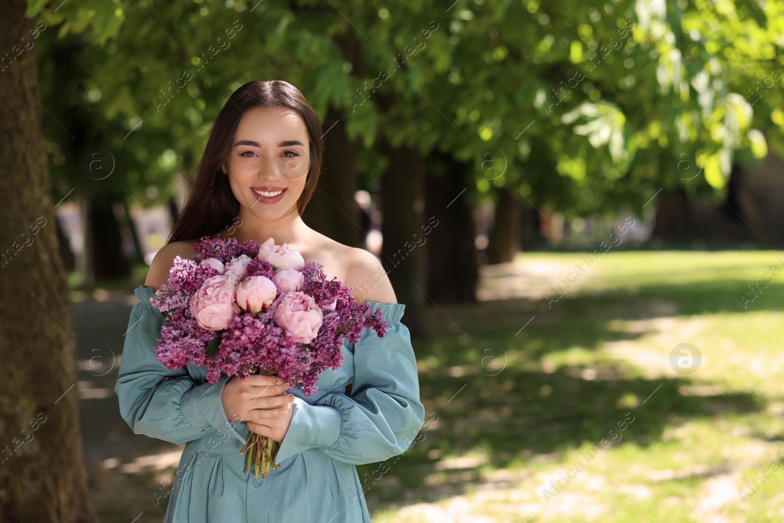 Photo of Beautiful woman with bouquet of spring flowers in park on sunny day, space for text