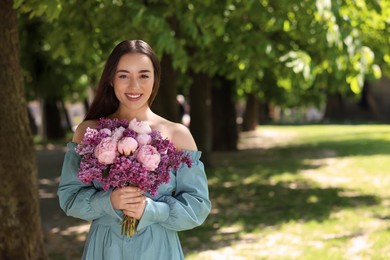 Beautiful woman with bouquet of spring flowers in park on sunny day, space for text