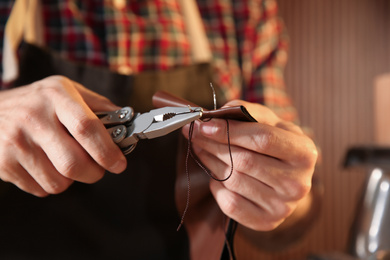 Man sewing piece of leather in workshop, closeup