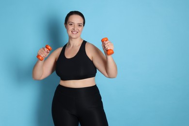 Photo of Happy overweight woman doing exercise with dumbbells on light blue background. Space for text