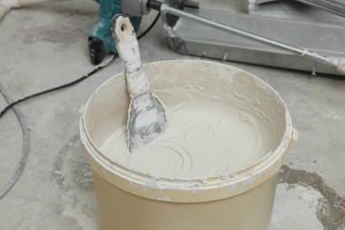 Photo of Bucket with plaster and putty knife on concrete floor, closeup