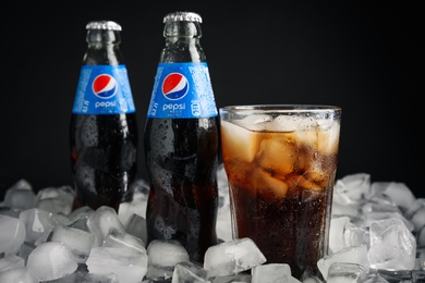 MYKOLAIV, UKRAINE - FEBRUARY 11, 2021: Glass of Pepsi and bottles on ice cubes against black background