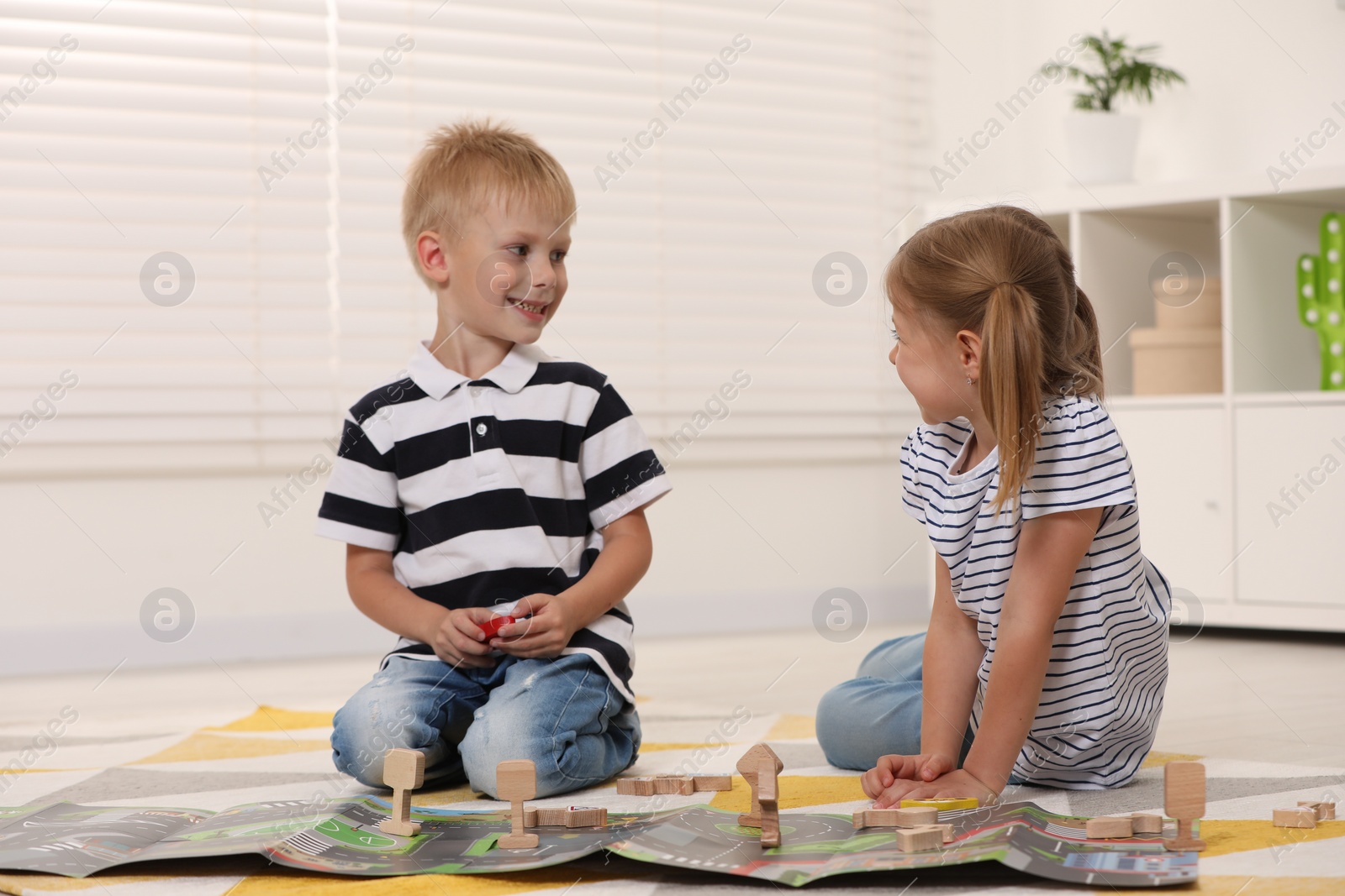 Photo of Little children playing with set of wooden road signs and toy cars indoors