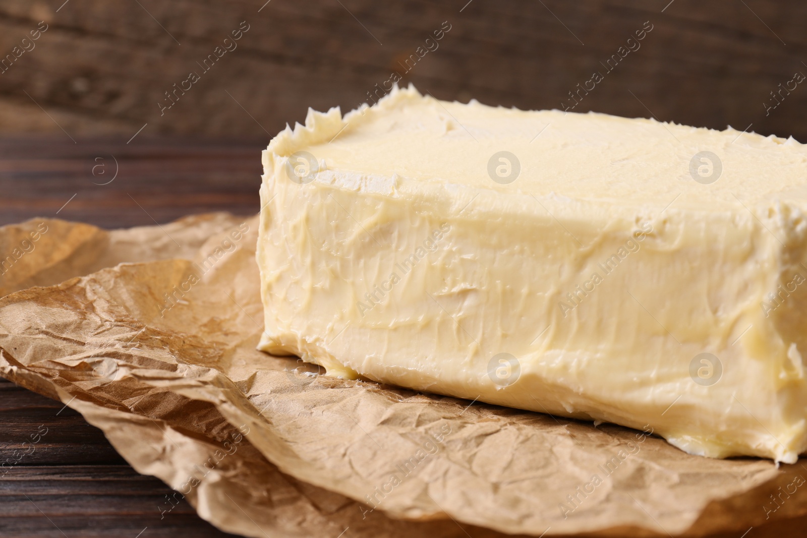 Photo of Parchment with piece of tasty homemade butter on wooden table, closeup