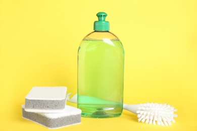 Photo of Detergent, brush and sponges on yellow background