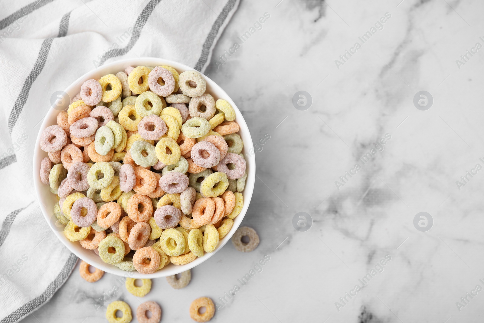 Photo of Tasty cereal rings in bowl on white marble table, top view. Space for text