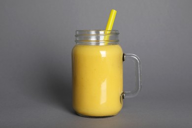 Mason jar of tasty smoothie with straw on grey background