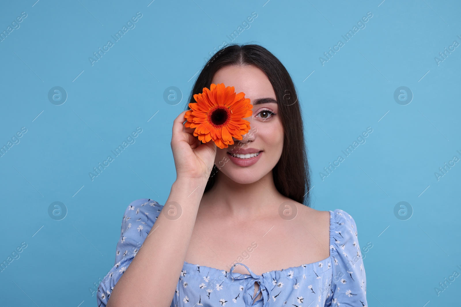 Photo of Beautiful woman with spring flower in hand on light blue background