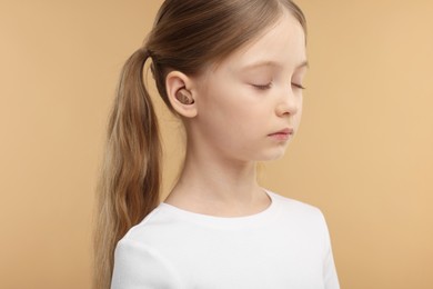 Little girl with hearing aid on pale brown background