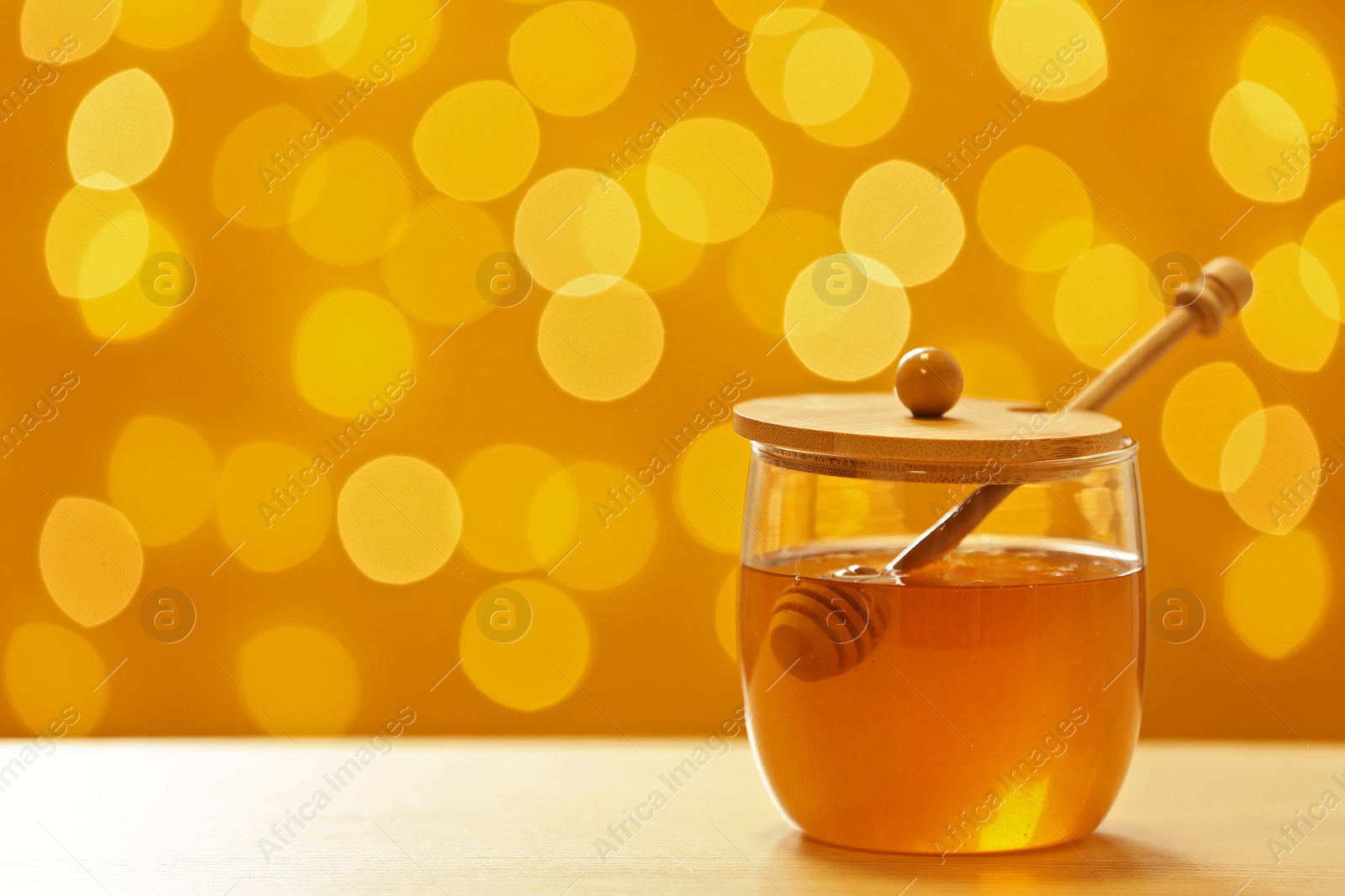 Photo of Jar with fresh honey on table against blurred background. Space for text