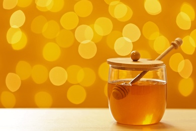 Jar with fresh honey on table against blurred background. Space for text