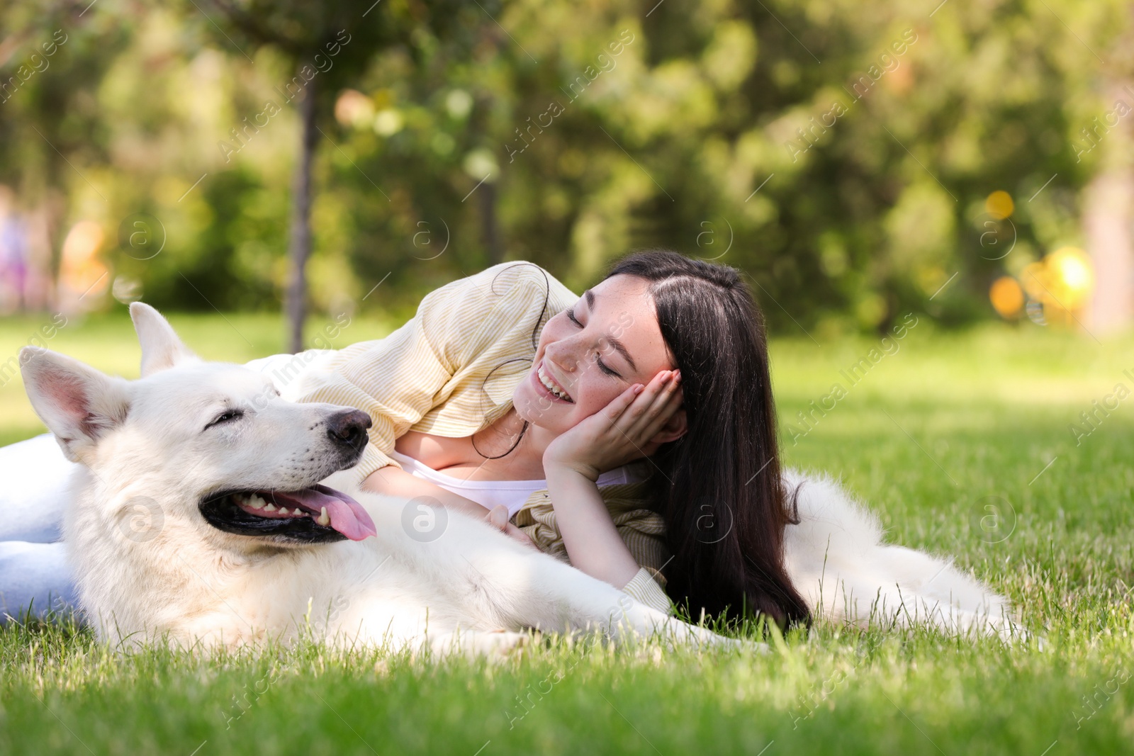 Photo of Teenage girl lying with her white Swiss Shepherd dog on green grass in park