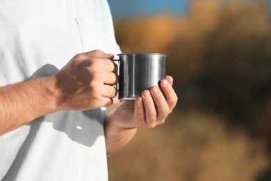 Photo of Male camper with metal mug outdoors, closeup. Space for text