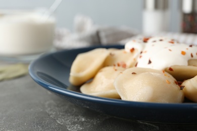 Photo of Delicious cooked dumplings with sour cream on grey table, closeup