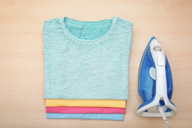 Photo of Folded clean clothes and iron on wooden background, top view