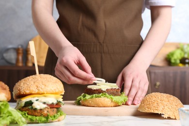 Photo of Woman making delicious vegetarian burger at white marble table, closeup